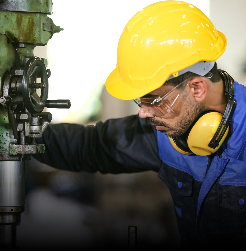 Manufacturing worker in yellow hard hat operating industrial machinery, representing production processes.