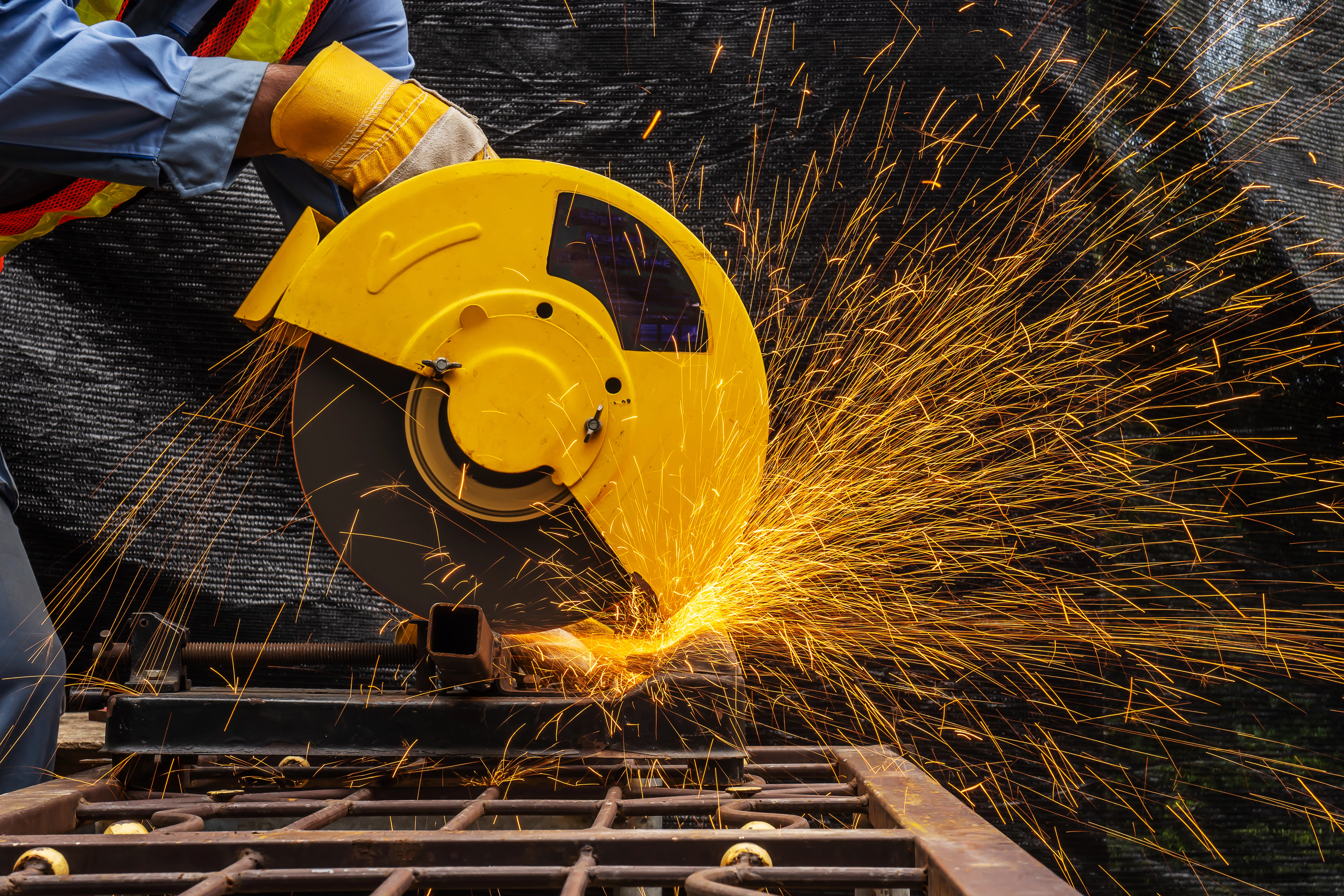 A metalworker wearing safety gear cuts metal with a circular saw, sparks flying.